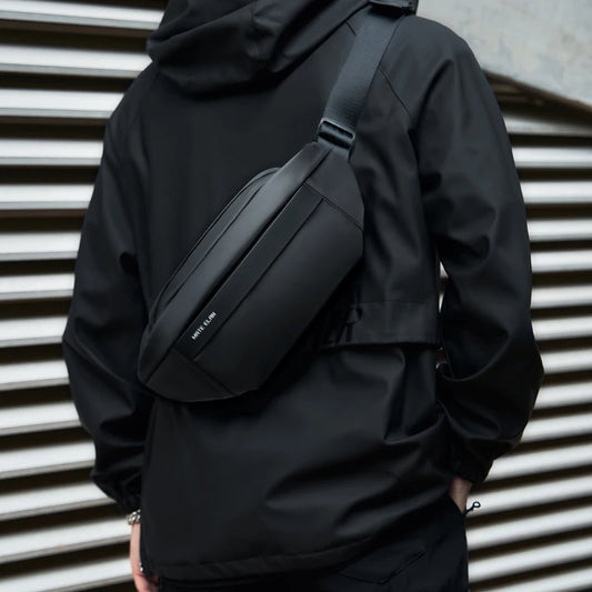 Person wearing a black jacket with a matching black waist bag against a metallic background