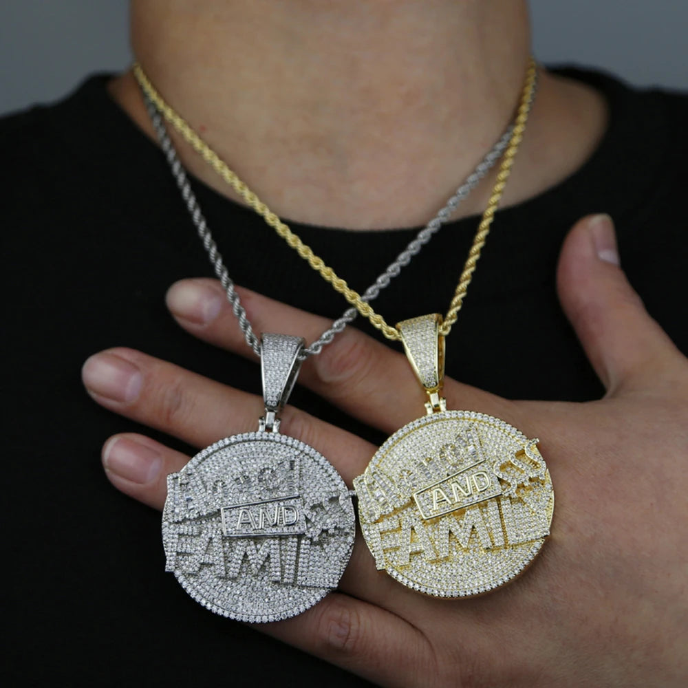 Two diamond-encrusted pendants, one silver and one gold, held by a person against a dark background.