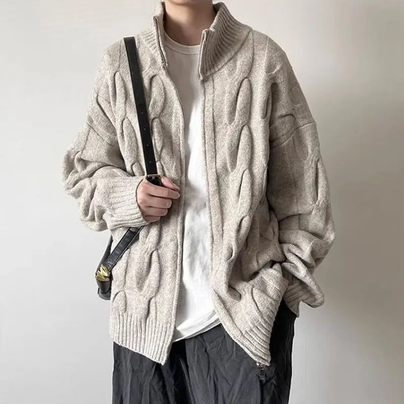 Person wearing a beige cable knit sweater over a white shirt with a plain background