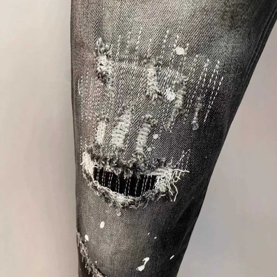Close-up of a black denim jeans leg with a large hole and ripped edges.