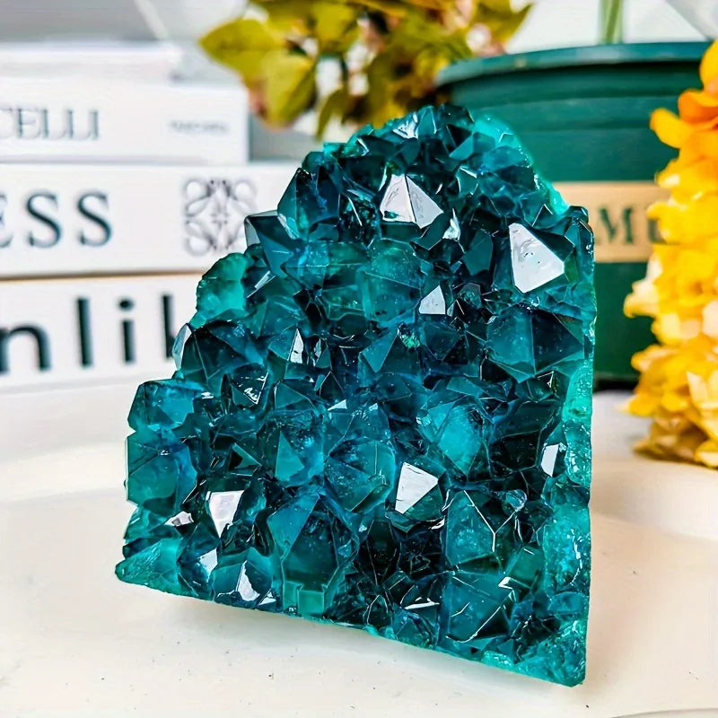 Teal crystal rock on a white surface with books and flowers in the background