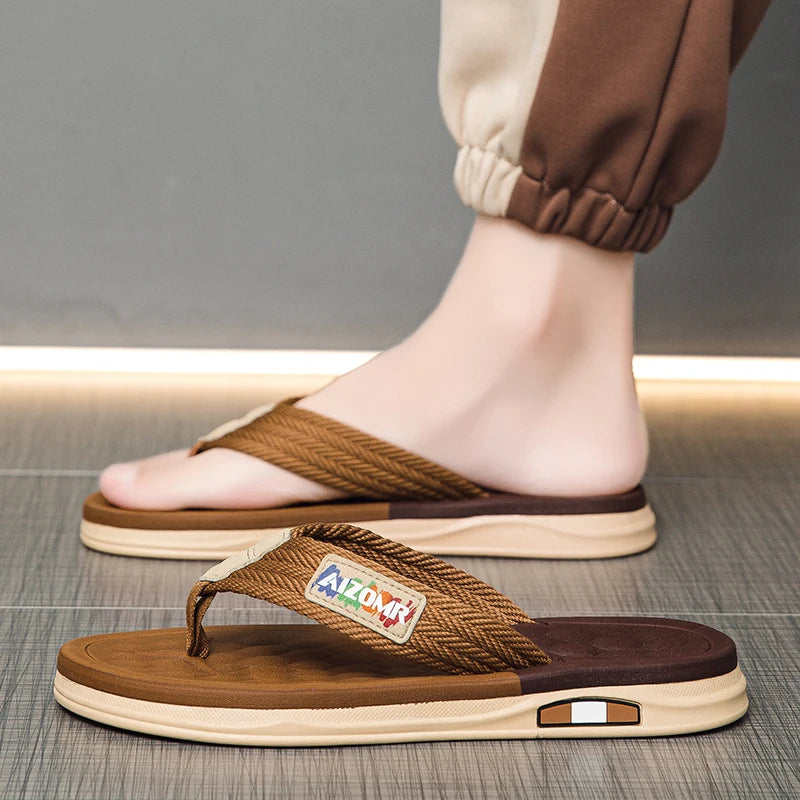 Brown sandals with a visible brand logo worn by a person on a gray floor.