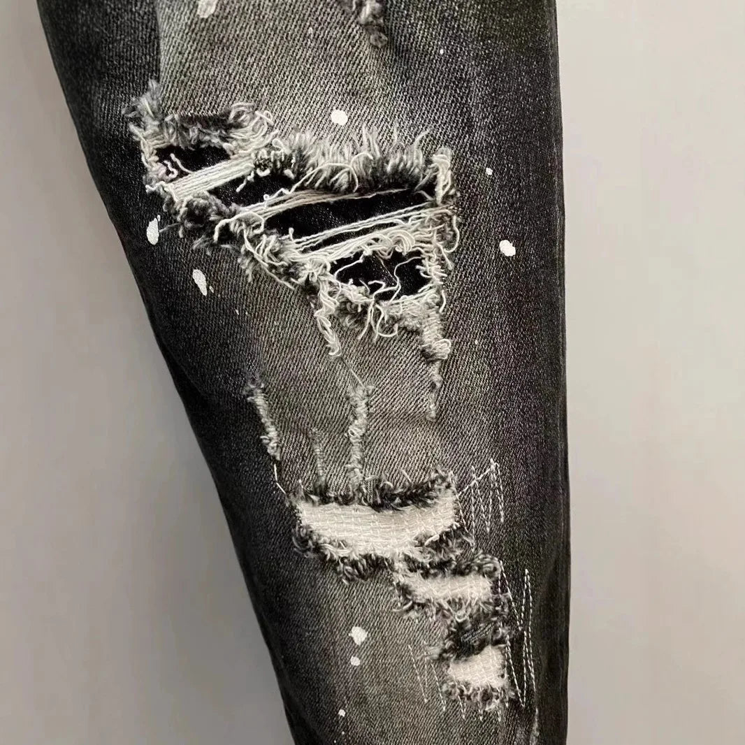 Distressed black denim jeans with a large hole in the knee area on a light gray background.