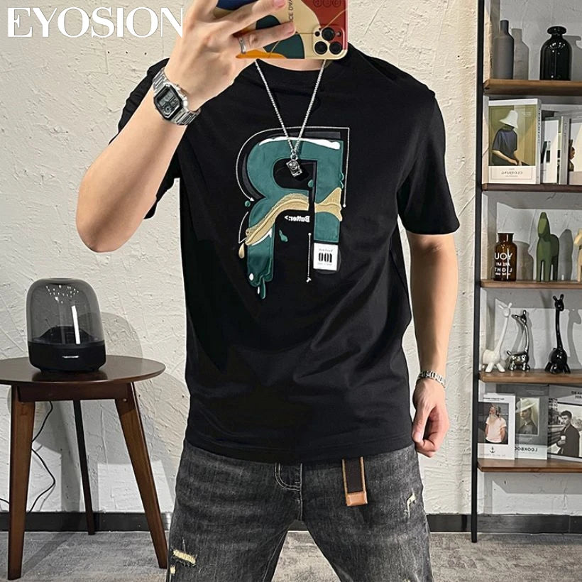 Person wearing a black t-shirt with a graphic design, standing in a room with a shelf and table.