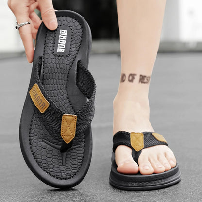 Black sandals with brown accents worn by a person on a gray surface