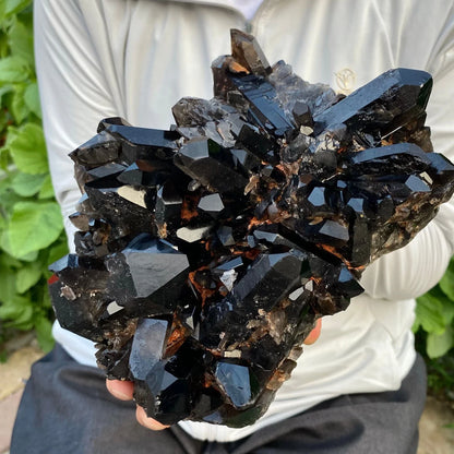 Person holding a large cluster of dark crystals outdoors