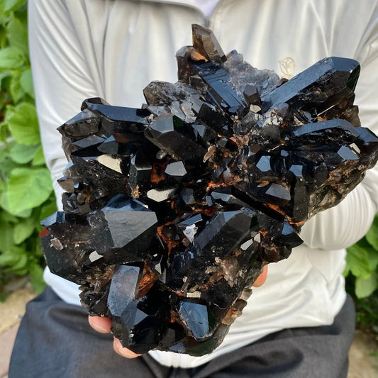 Person holding a large cluster of dark crystals outdoors