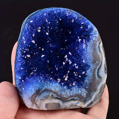 Blue geode crystal held in a hand against a black background