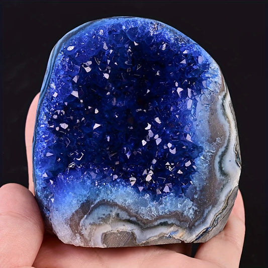 Blue geode crystal held in a hand against a black background