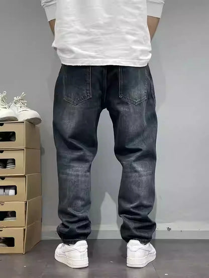 Person wearing dark jeans and white sneakers standing against a plain background