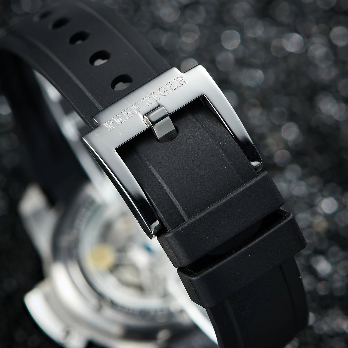 Close-up of a black watch strap with a silver buckle on a blurred background