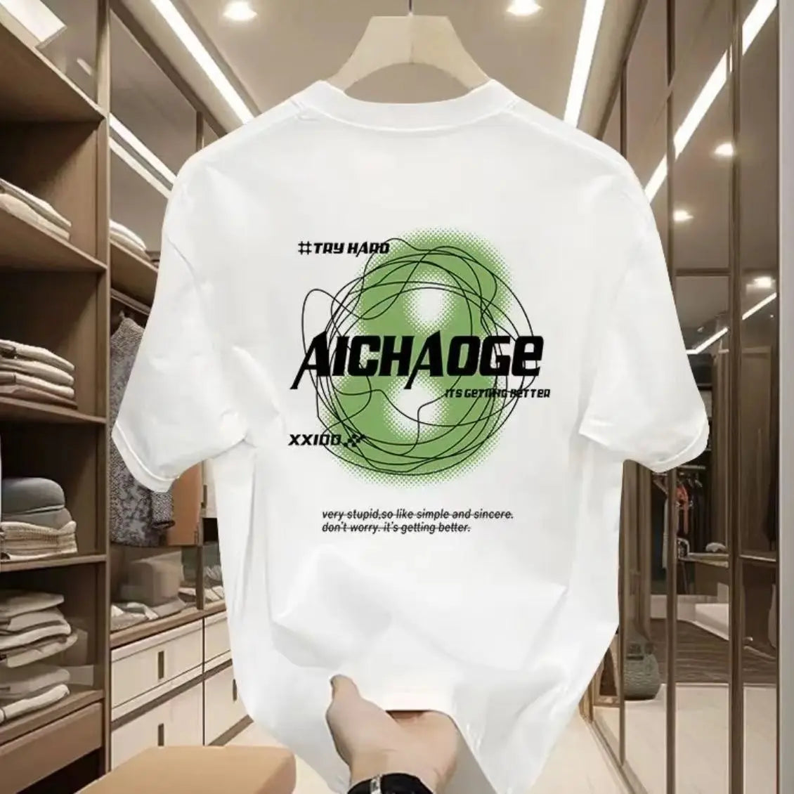 White t-shirt with green and black graphics and text on a hanger in a room.