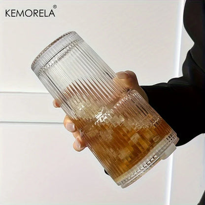 Hand holding a ribbed glass with a drink, brand 'KEMORELA' visible