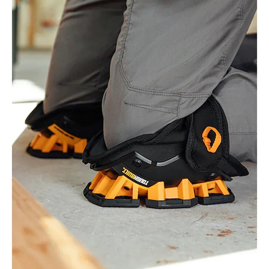 Black and orange work boots with unique sole design worn by a person on a concrete floor.