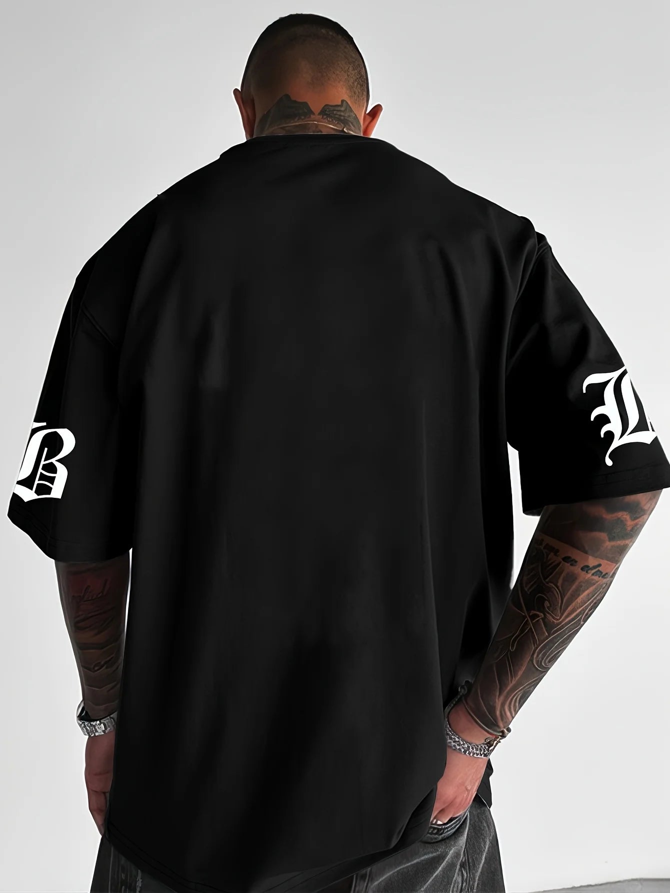 Person wearing a black t-shirt with visible brand logos on sleeves against a plain background