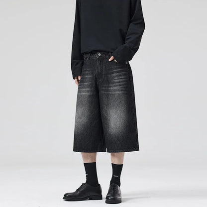 Person wearing black denim shorts and black shoes on a white background