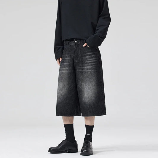 Person wearing black denim shorts and black shoes on a white background