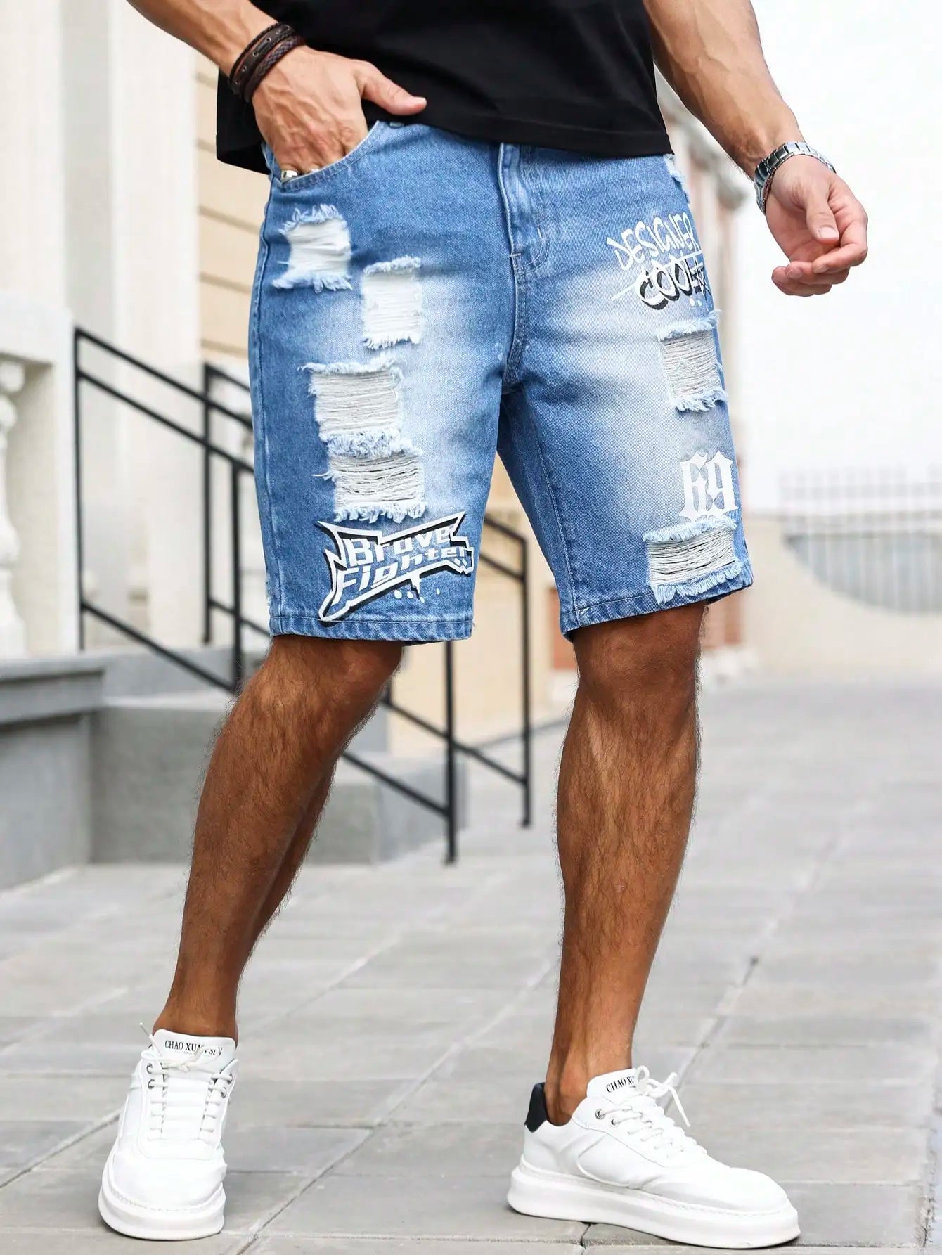 Person wearing blue ripped denim shorts with branding, standing on a sidewalk.