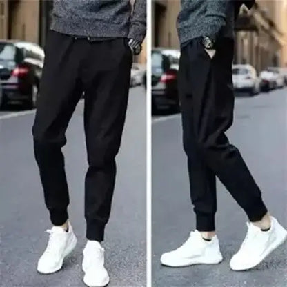 Person wearing black jogger pants and white sneakers on a street.