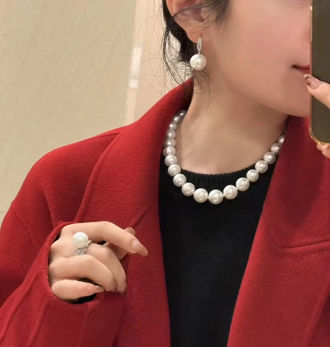 Person wearing a pearl necklace, earrings, and ring with a red coat and black top.