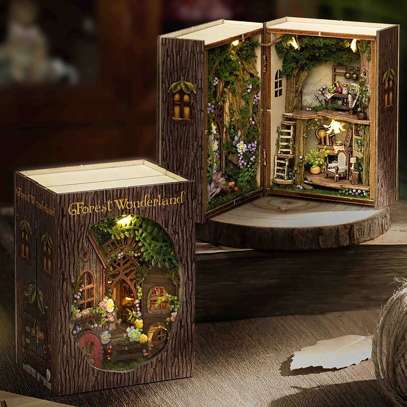 Wooden book-shaped box with a miniature fairy tale scene inside, featuring a small house and garden.