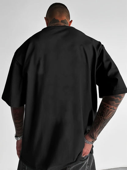 Person wearing a black t-shirt with tattoos on arms and neck against a plain background