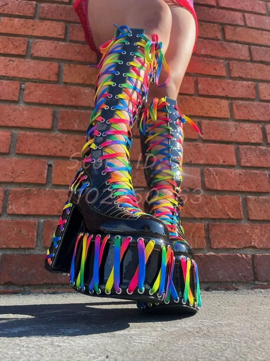 Colorful knee-high boots with fringe detail worn by a person against a brick wall.