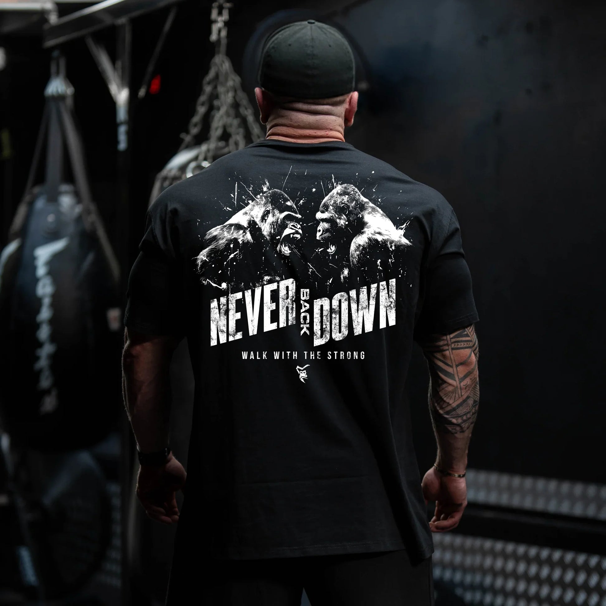 Person wearing a black t-shirt with 'Never Back Down' text and mountain graphic, standing in a dark room.