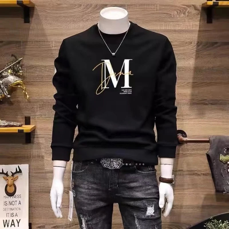 Black hoodie with gold letter 'M' on a mannequin against a wooden wall.