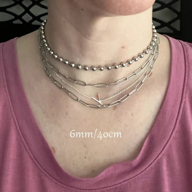 Person wearing multiple silver necklaces on a plain background
