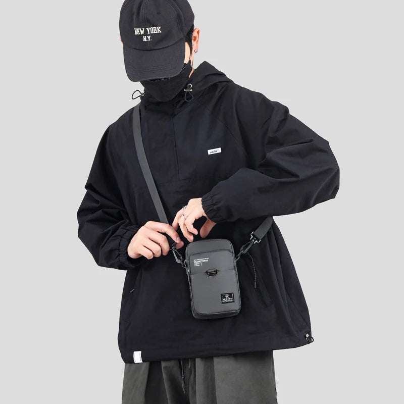 Person wearing a black jacket and cap, holding a gray crossbody bag on a light gray background