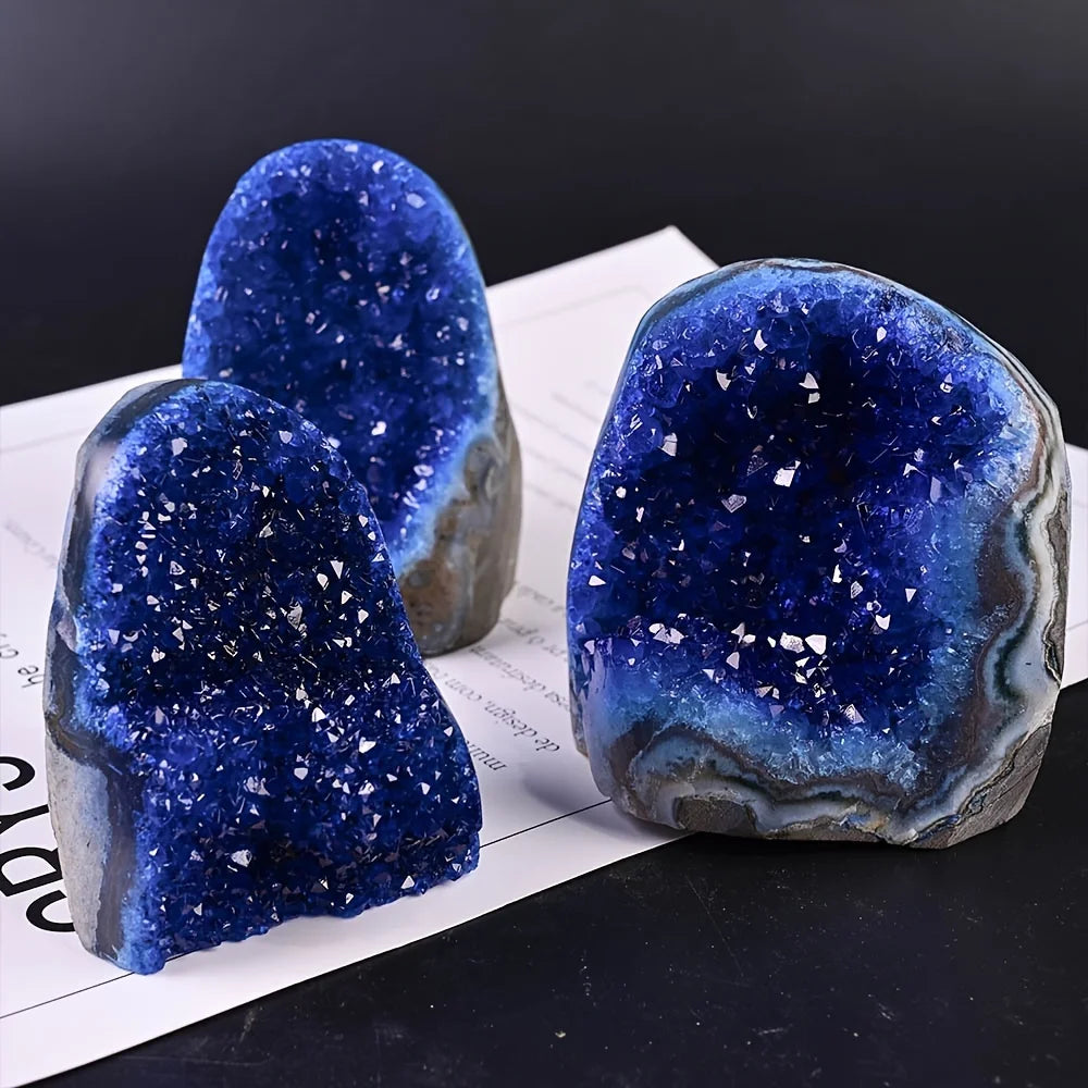 Three blue geode crystals on a black surface with a dark background