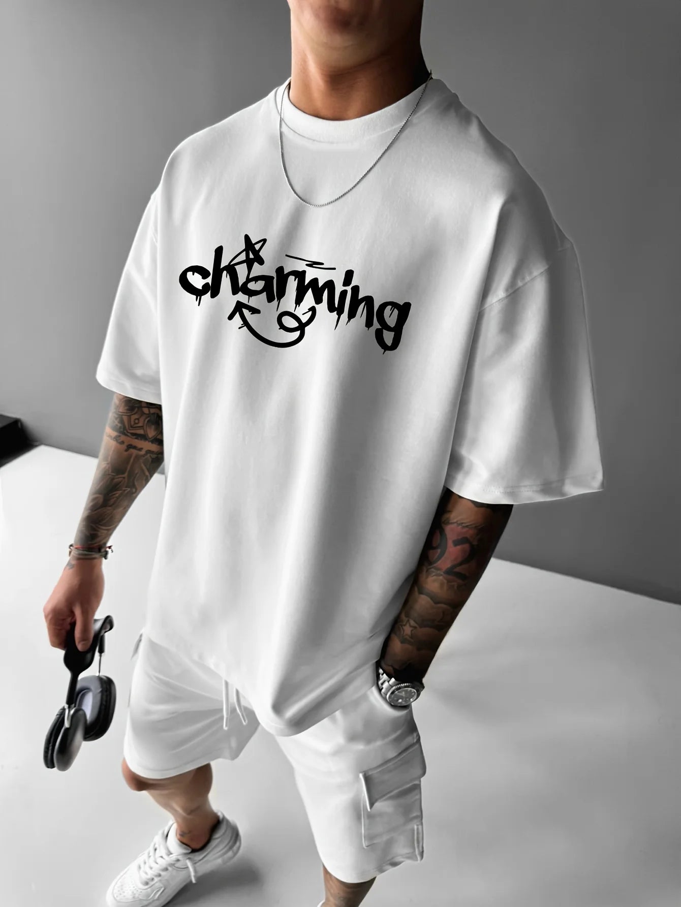 Person wearing a white t-shirt with 'charming' text, holding sunglasses, on a gray background