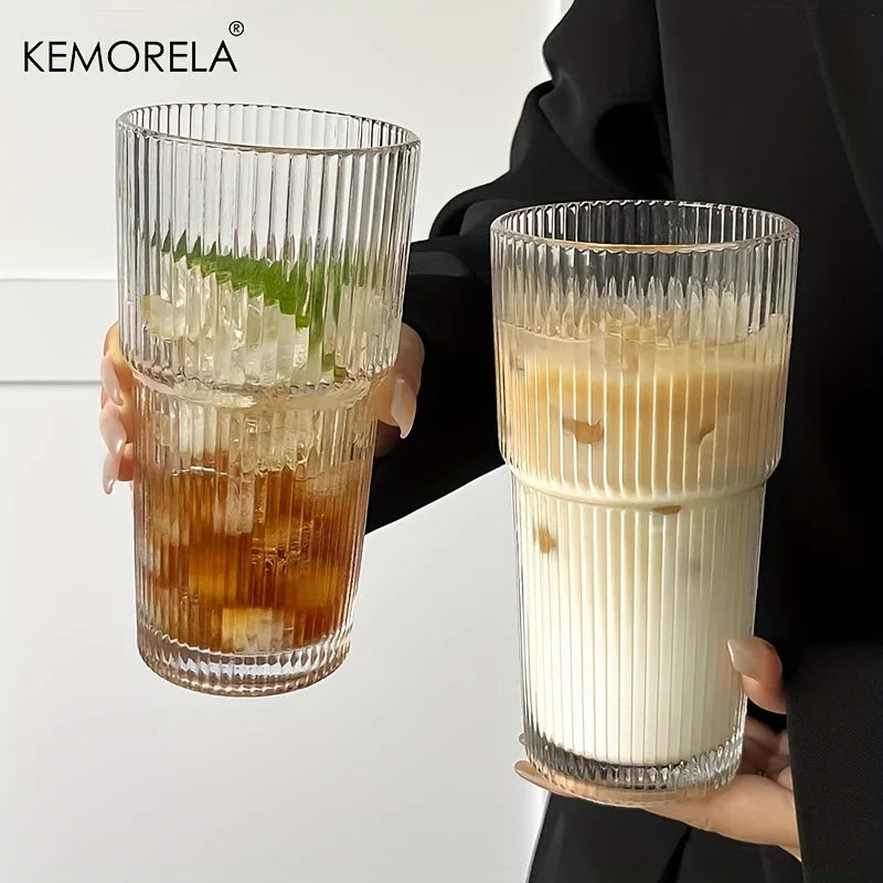Two hands holding glasses with iced beverages against a neutral background