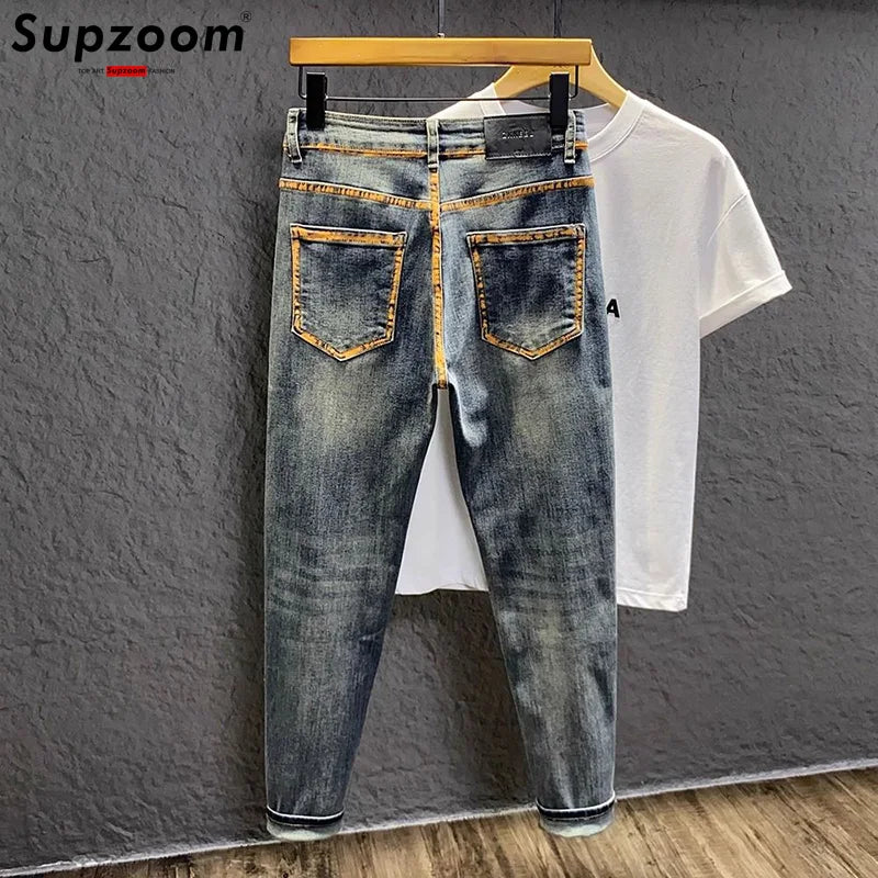 Blue jeans and white t-shirt on a hanger against a gray wall with 'Supzoom' branding.