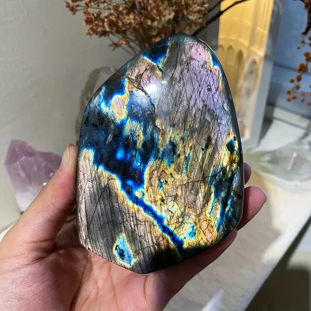 Hand holding a colorful labradorite stone with a blurred indoor background