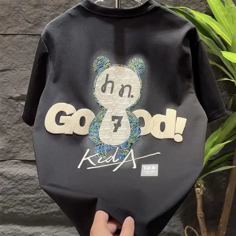 Black t-shirt with a graphic design and text held against a stone wall.