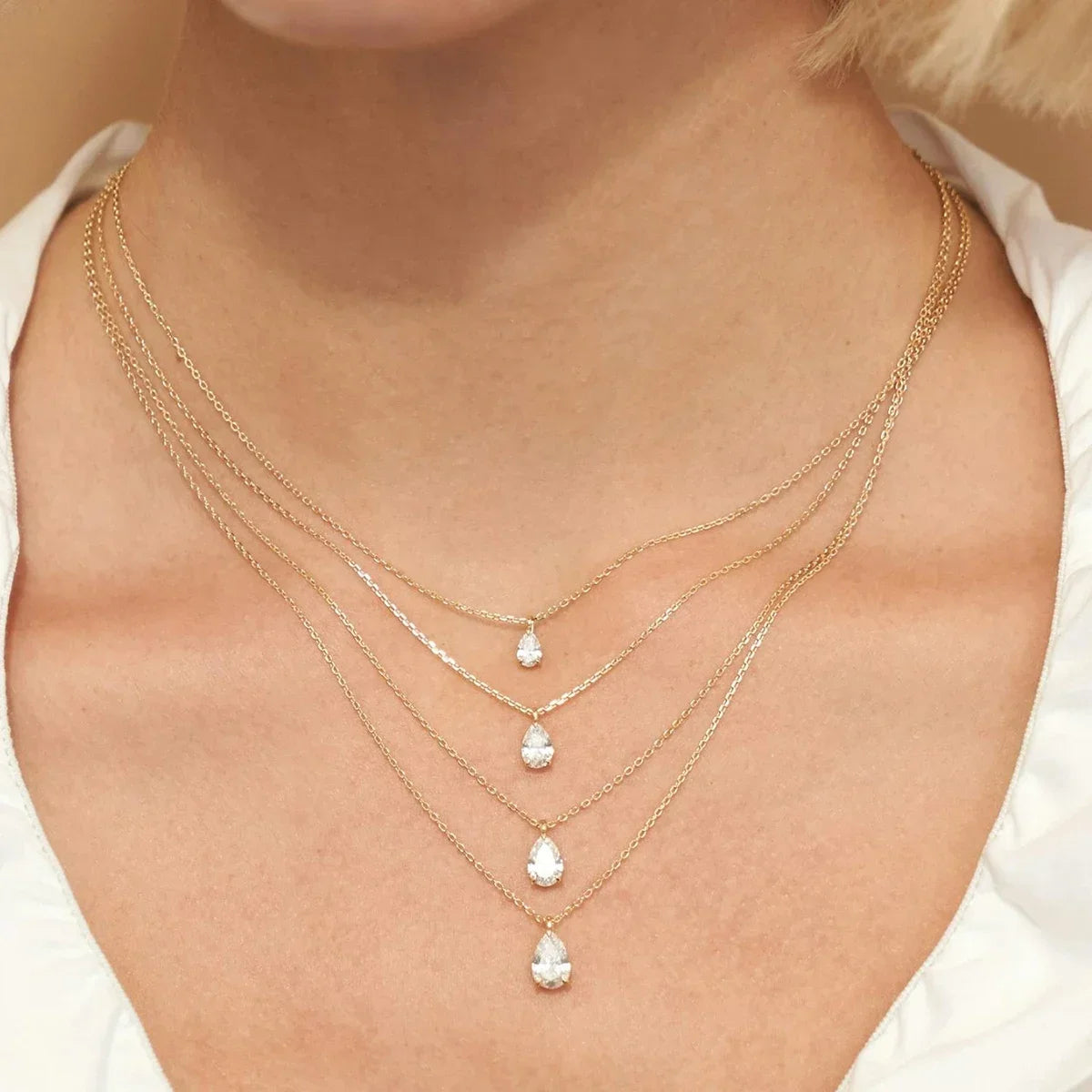 Close-up of a person wearing multiple gold necklaces with teardrop-shaped pendants.