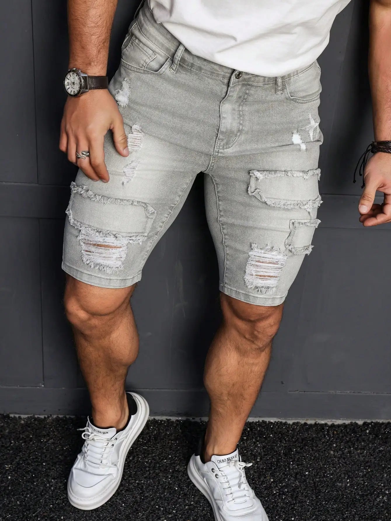 Person wearing light gray distressed denim shorts with white sneakers against a dark background