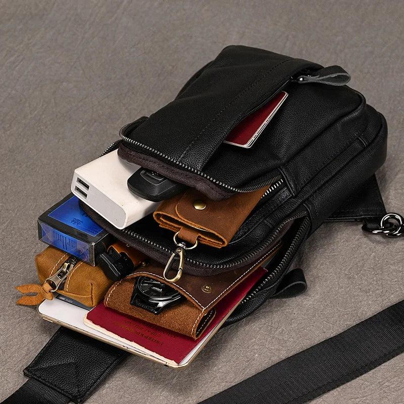 Black crossbody bag with various compartments and items on a gray surface