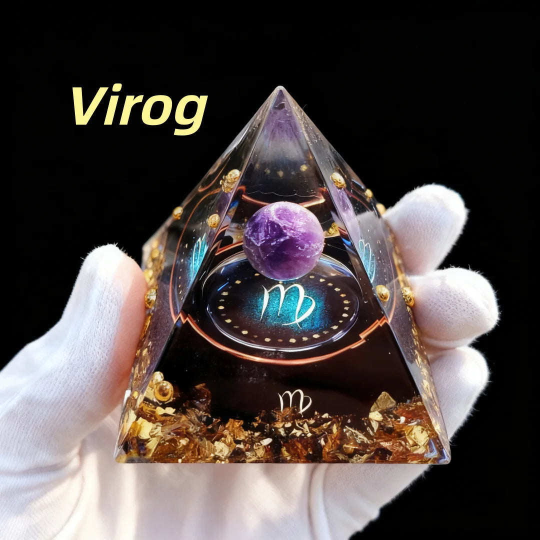 Pyramid-shaped decorative item with a purple sphere and gold elements, held by a gloved hand against a black background. Brand 'Virog' visible.