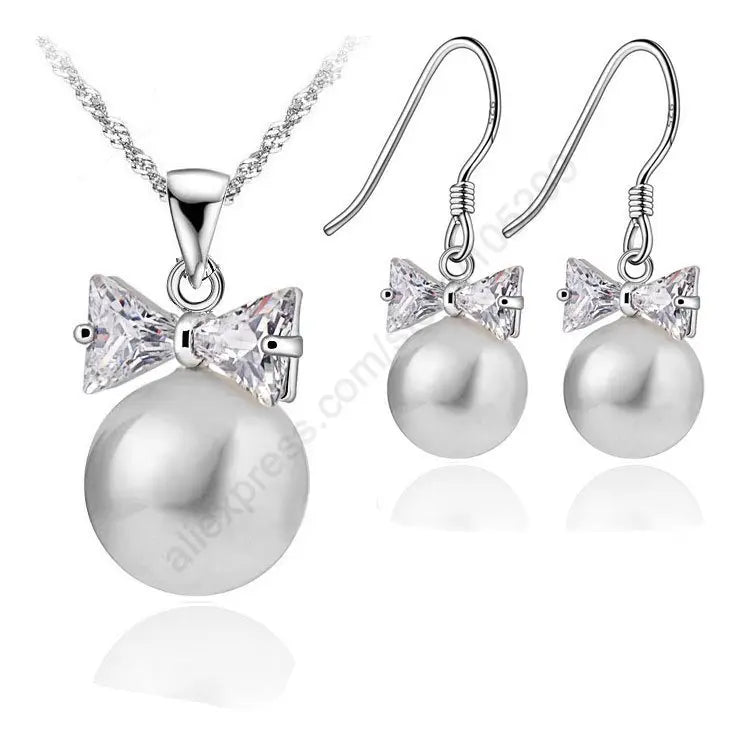 Pearl necklace and earrings set with bow and crystal details on a white background