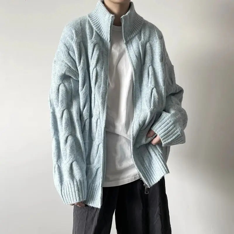Person wearing a light blue knitted cardigan over a white shirt with a plain background