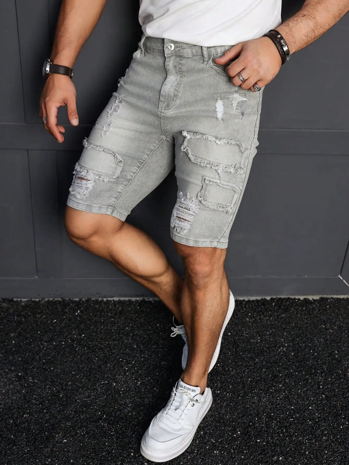 Person wearing gray distressed shorts and white sneakers against a dark background