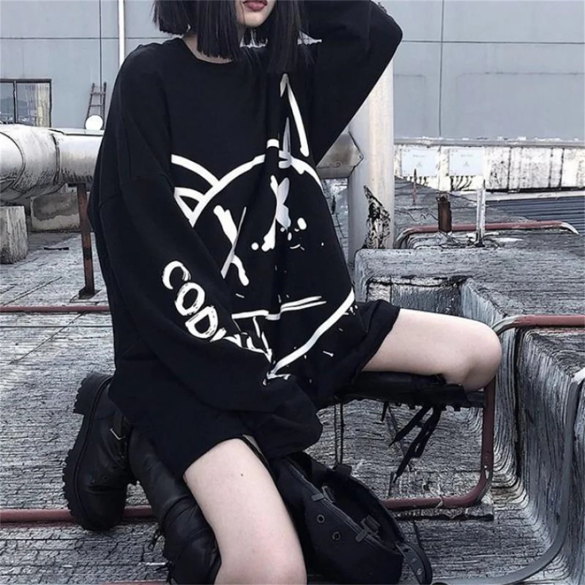 Person wearing a black oversized sweatshirt with white text, sitting on a rooftop.