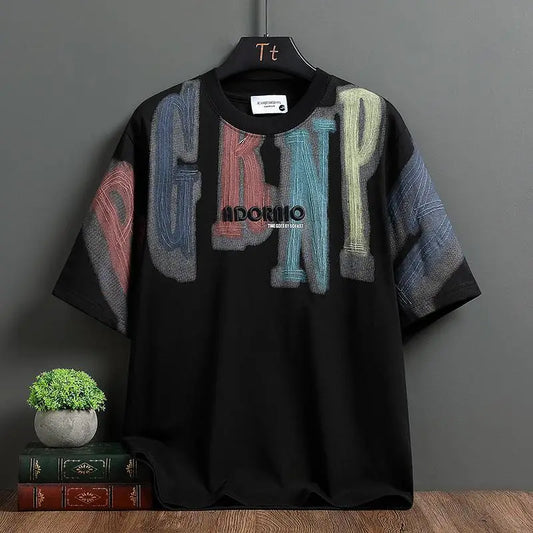 Black t-shirt with colorful text design on a hanger against a gray wall.