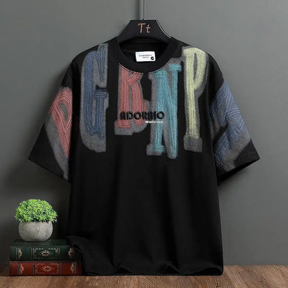 Black t-shirt with colorful text design on a hanger against a gray wall.