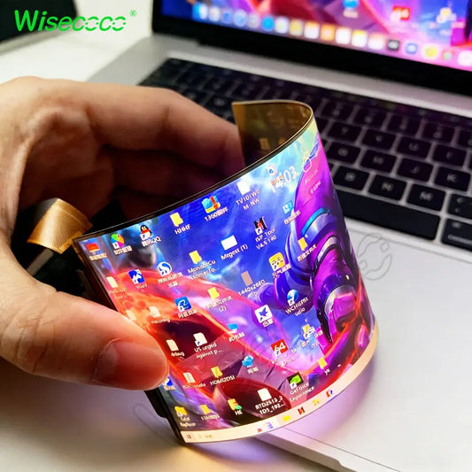 Hand holding a flexible smartphone with a colorful display in front of a laptop.