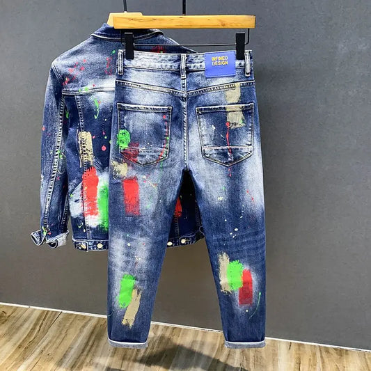 Blue jeans with paint splatter design on a wooden hanger against a gray wall.
