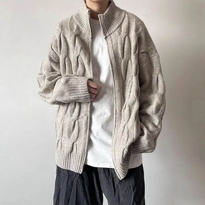 Person wearing a beige cable knit cardigan over a white shirt with a plain background